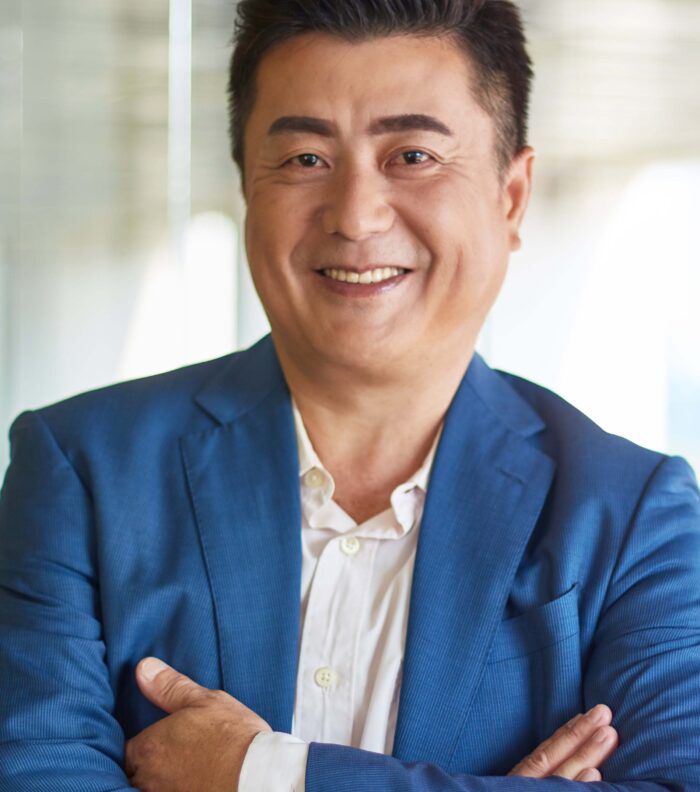 Portrait of older Asian executive with arms folded standing in his office.