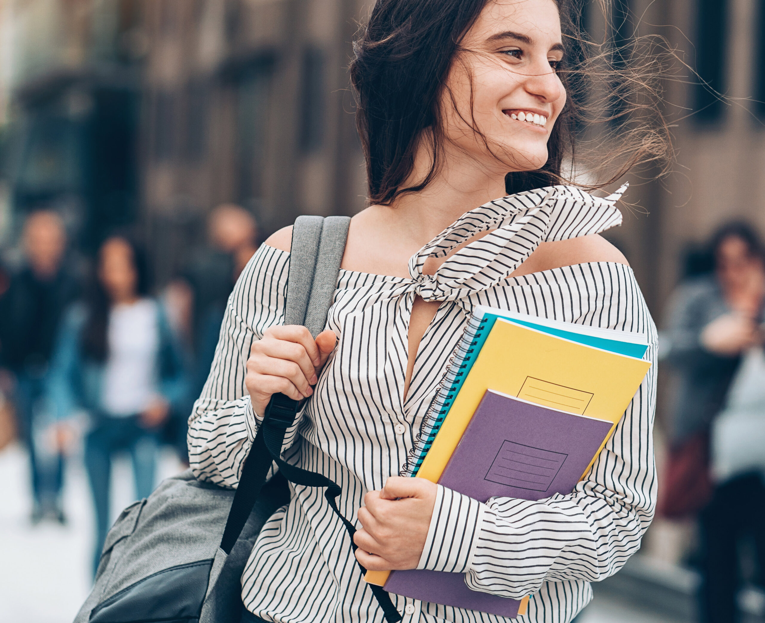 Smiling woman carries her books through campus.