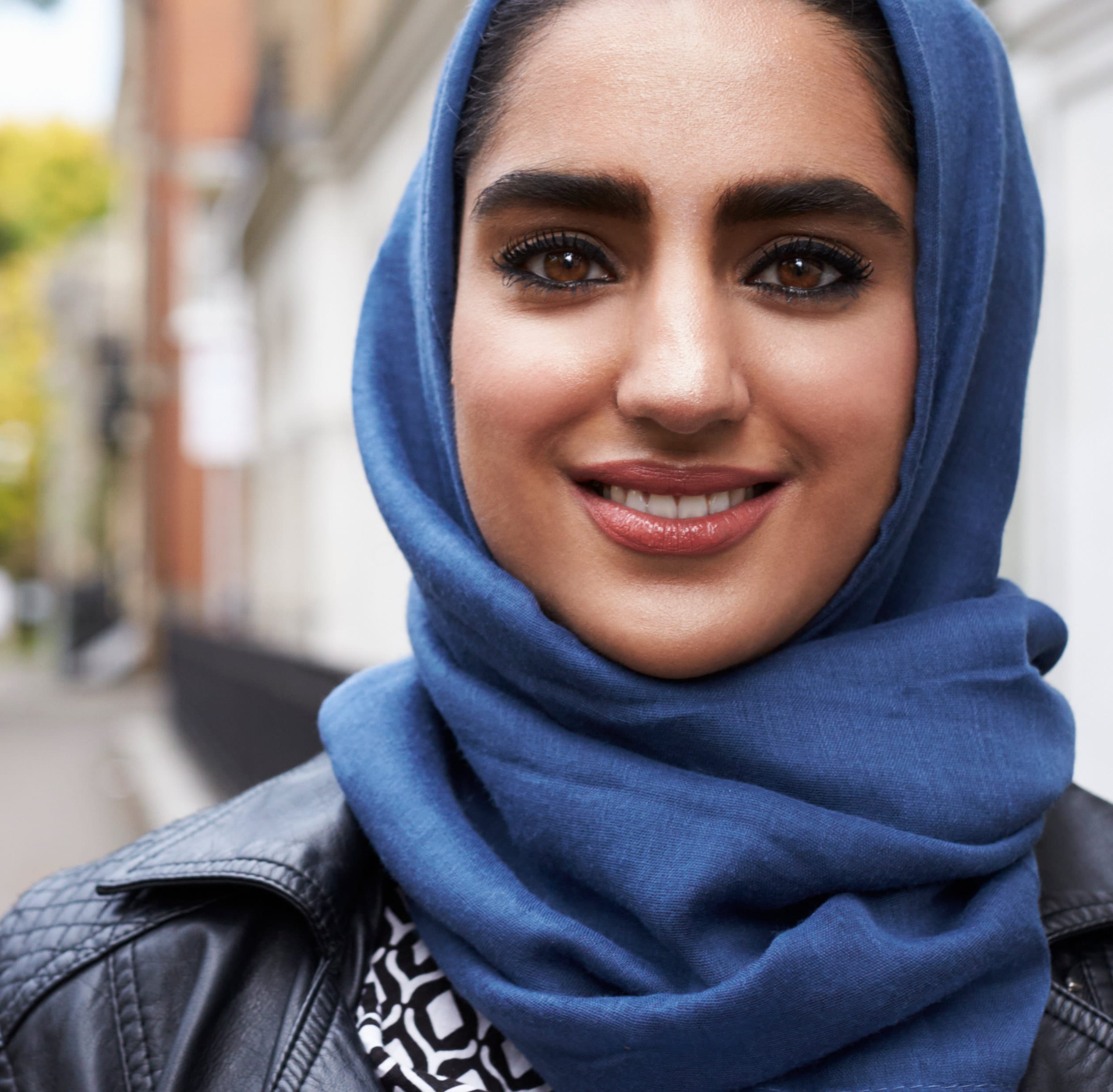 Portrait of a smiling woman with a hijab standing on a city street.